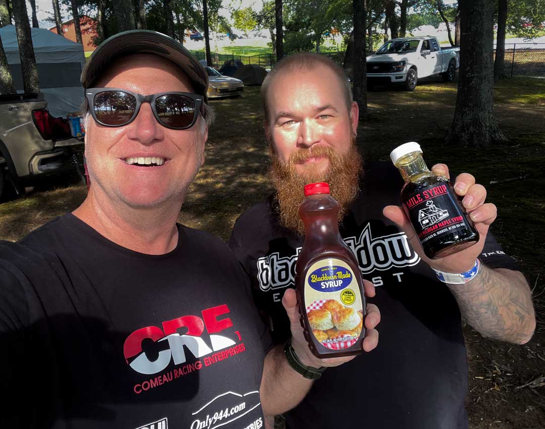 Two 944Fest campers holding up bottles of local syrup at the Sunday Syrup Swap